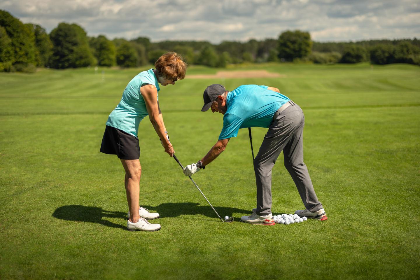 A golf instructor assists a woman with her swing on a green golf course.