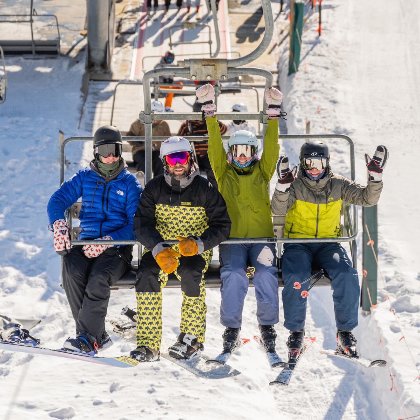 Skiers on a chairlift, wearing colorful winter gear, snowy background.