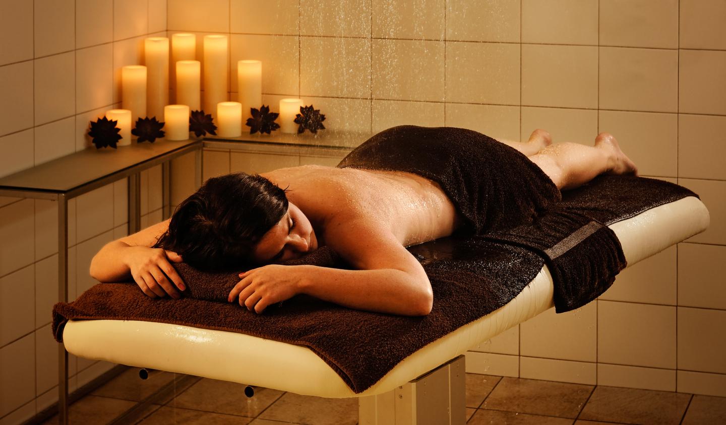 Person relaxing face down on a massage table, surrounded by lit candles.
