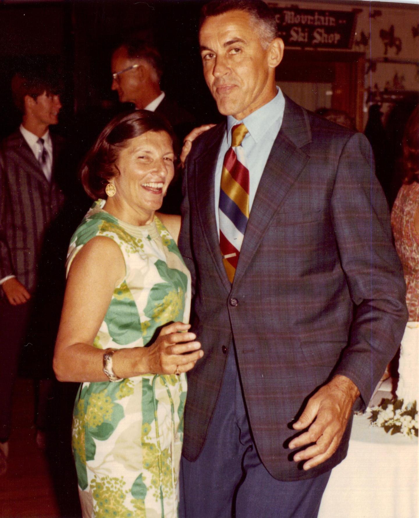 Smiling couple dancing at a formal event, woman in floral dress, man in plaid suit.