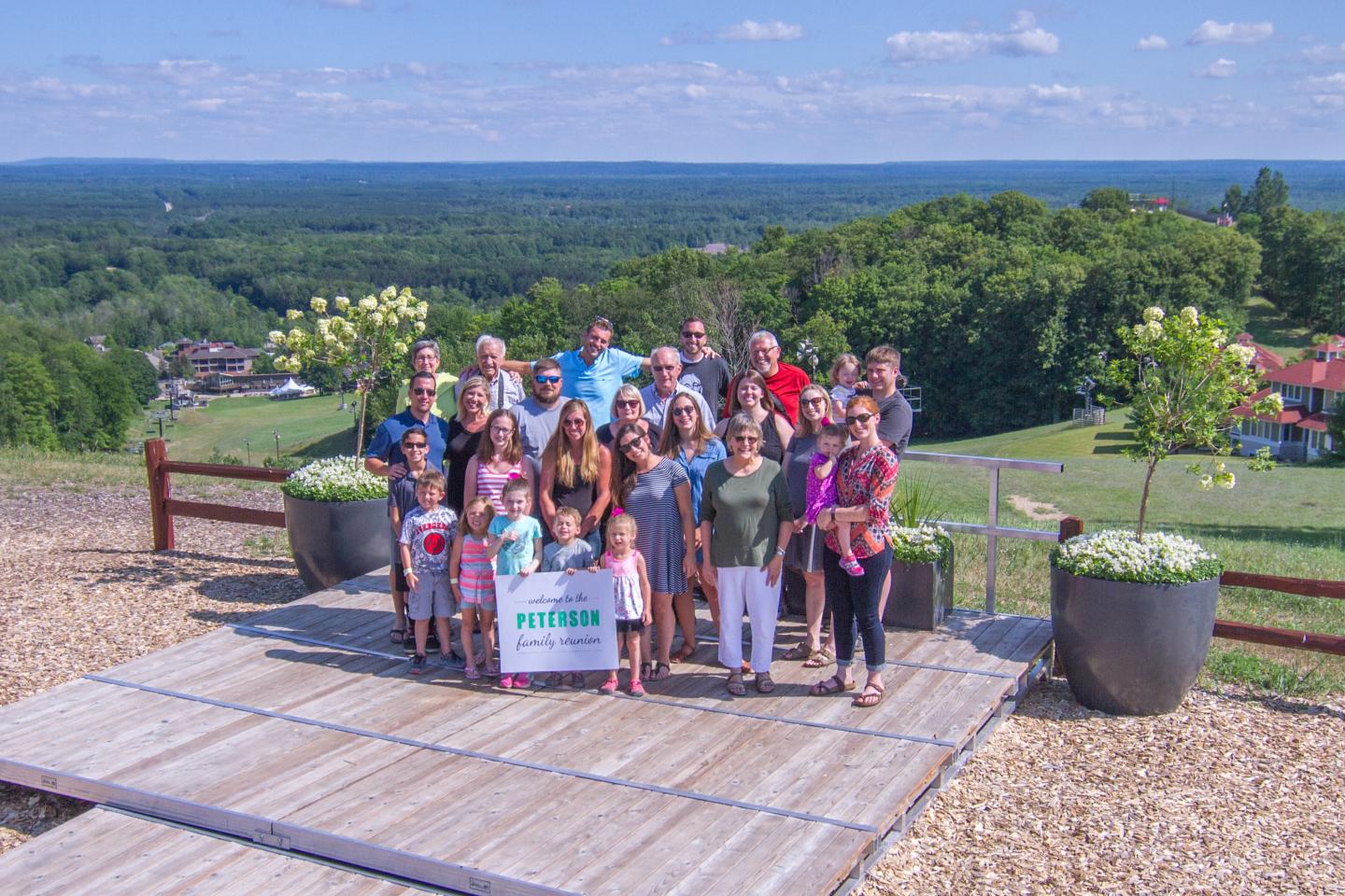 A group of people poses on a wooden platform overlooking a lush, green landscape.
