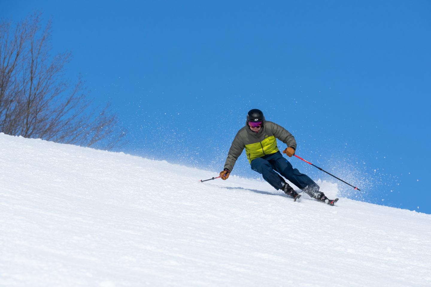 Skier in motion on a snowy slope under a clear blue sky.