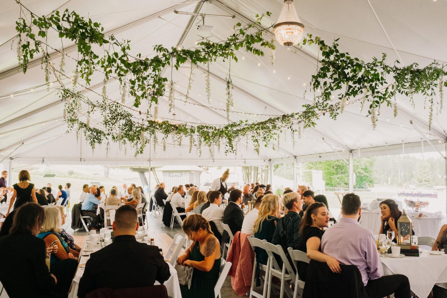 Wedding reception in a decorated tent with guests seated at tables.