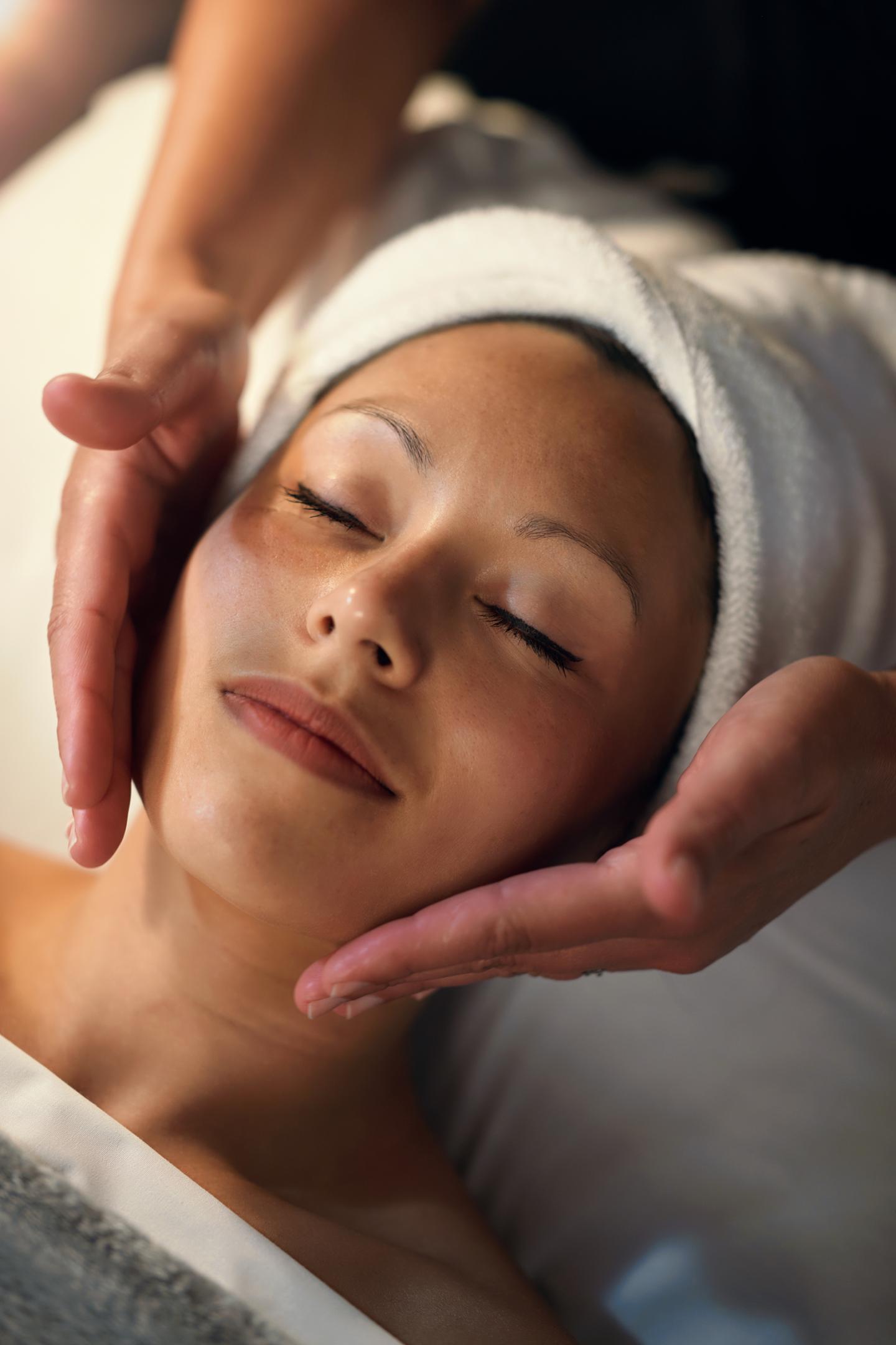 Person receiving a facial massage, eyes closed, with a towel wrapped around their head.