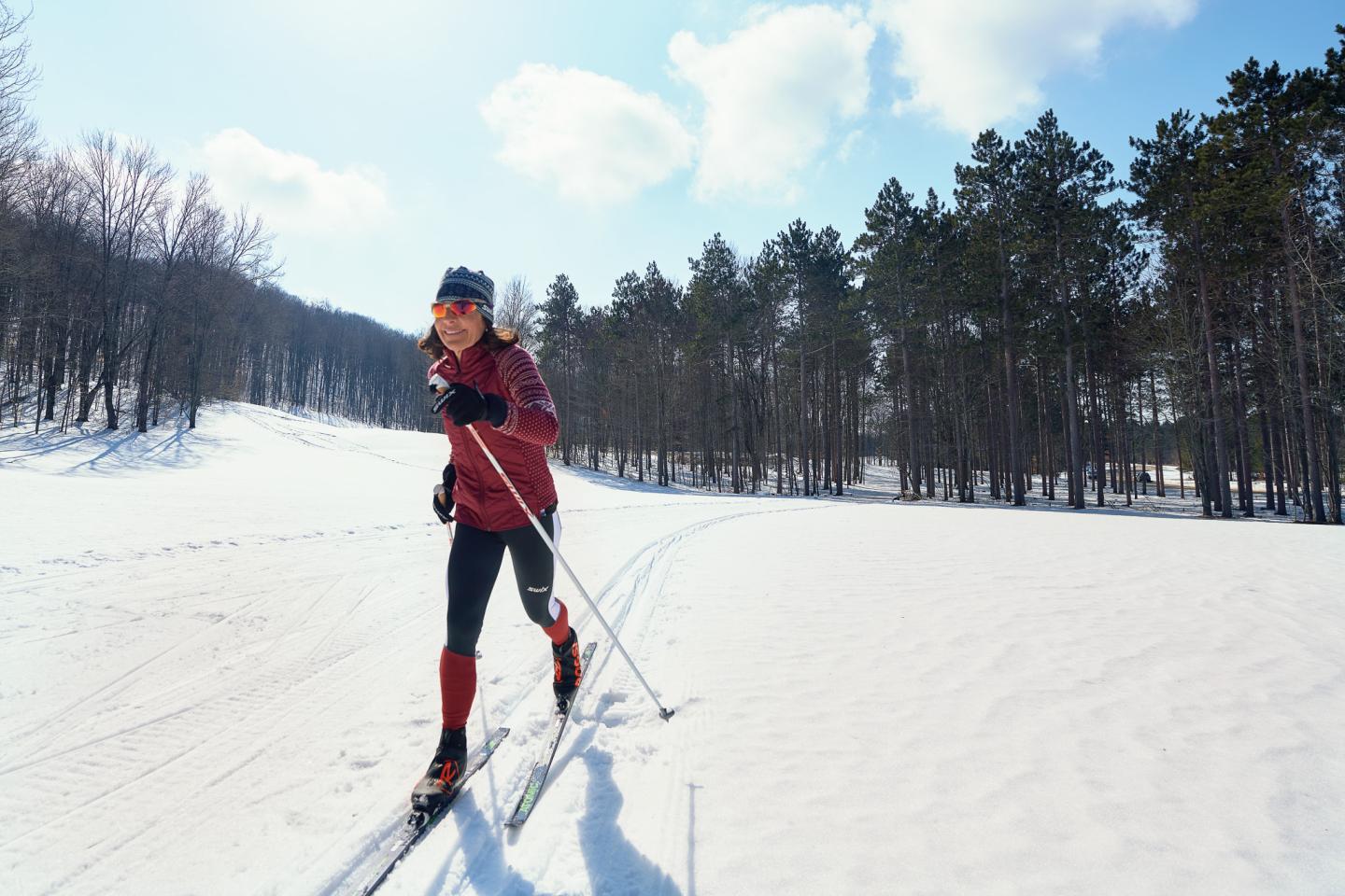 Person cross-country skiing through snowy forest in sunlight.