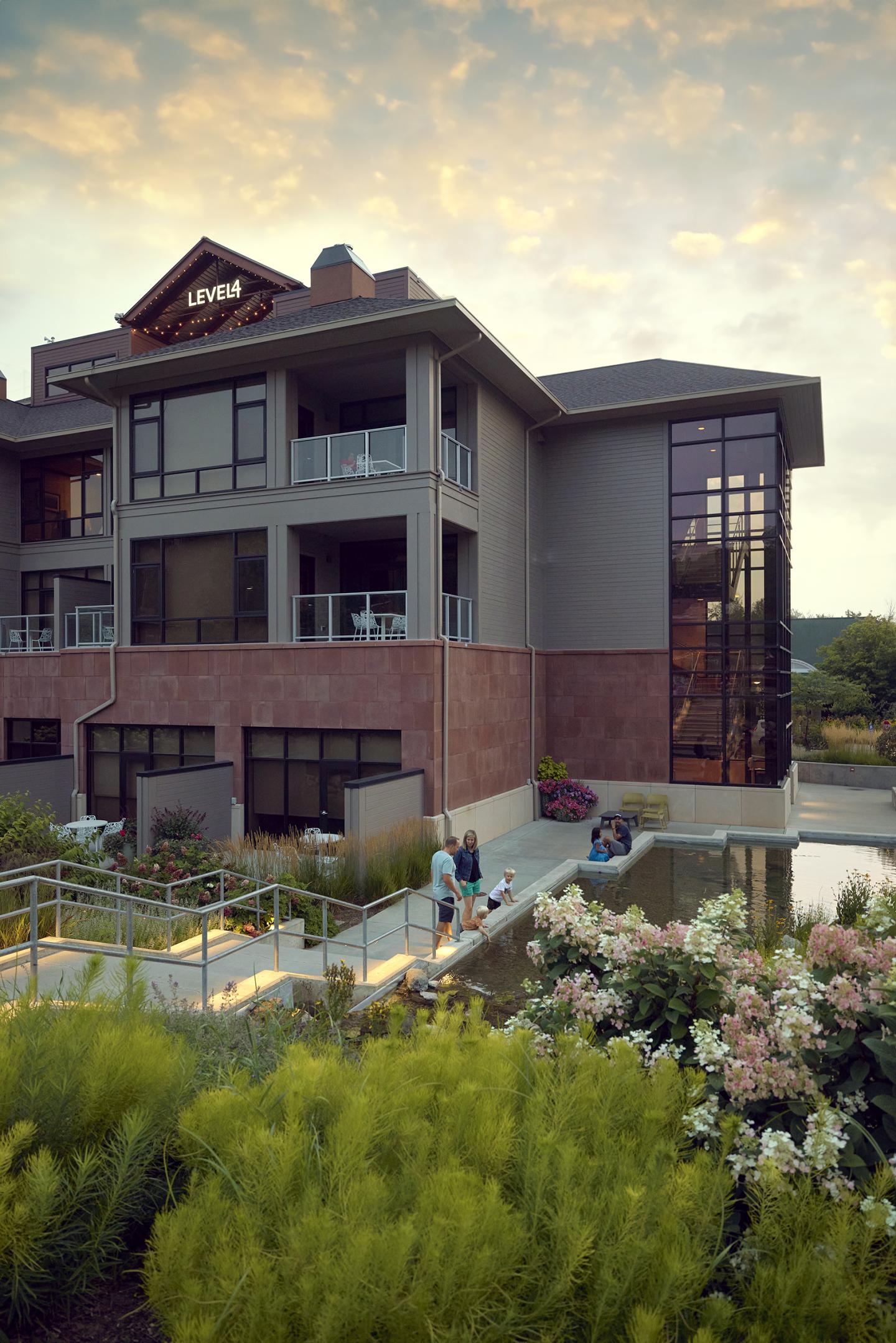 Modern building with large windows and balconies, surrounded by gardens at sunset.