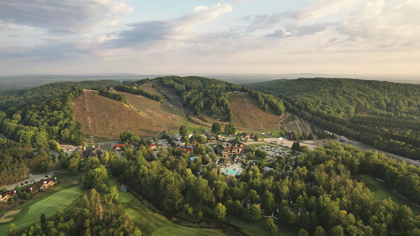 Aerial view of a lush valley with buildings surrounded by green hills and trees.