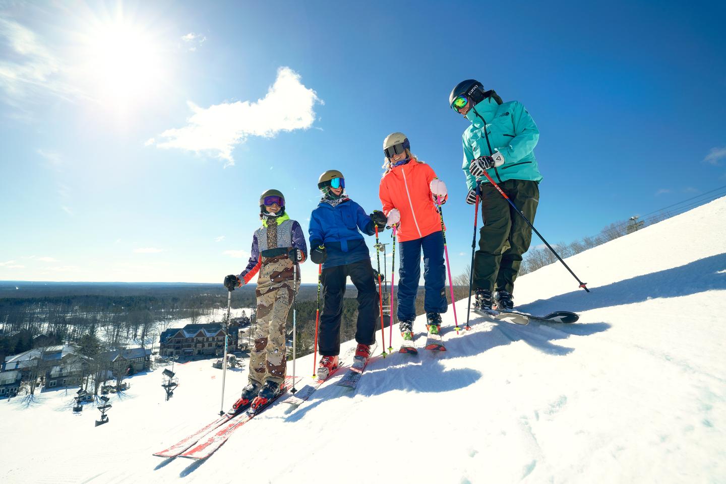 Group of four skiers posed on a snowy slope under a clear blue sky.