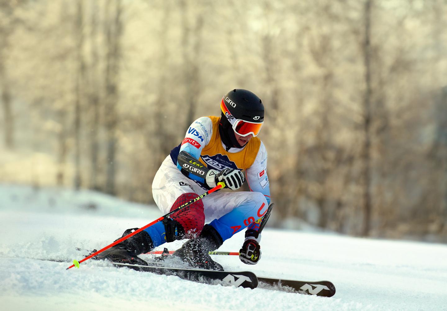 Skier racing downhill on snowy slope, wearing helmet and goggles.