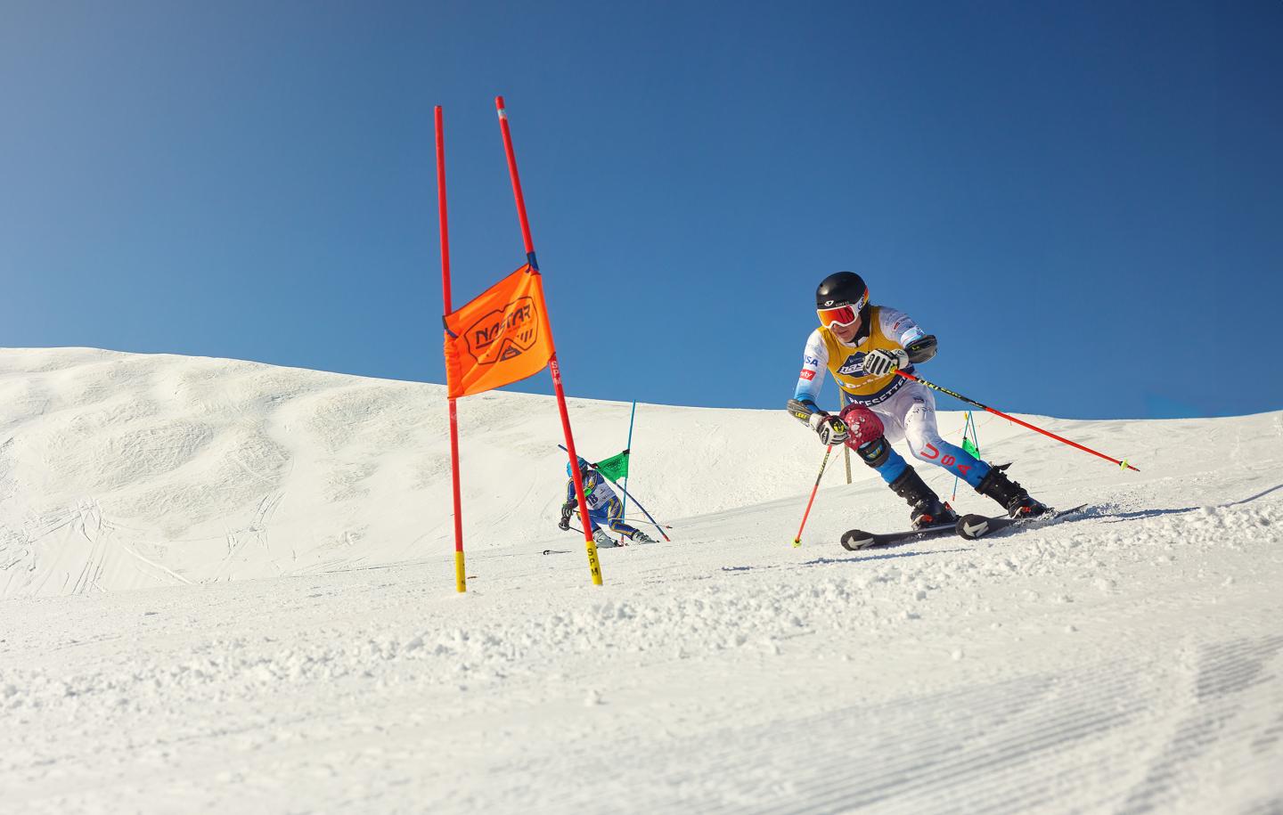 Ski racer navigating a slalom course under a clear blue sky.