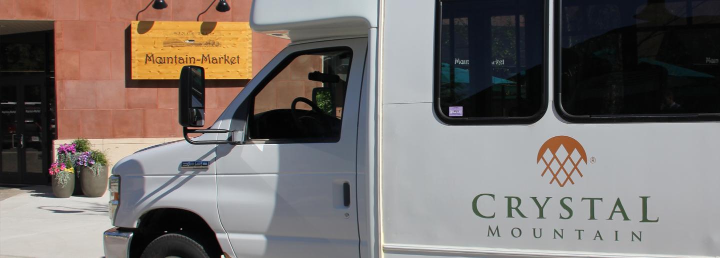 White "Crystal Mountain" shuttle bus parked outside a building.