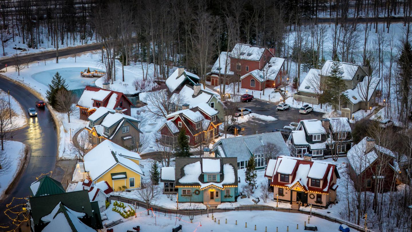 Snow-covered village with colorful houses surrounded by trees and a winding road.