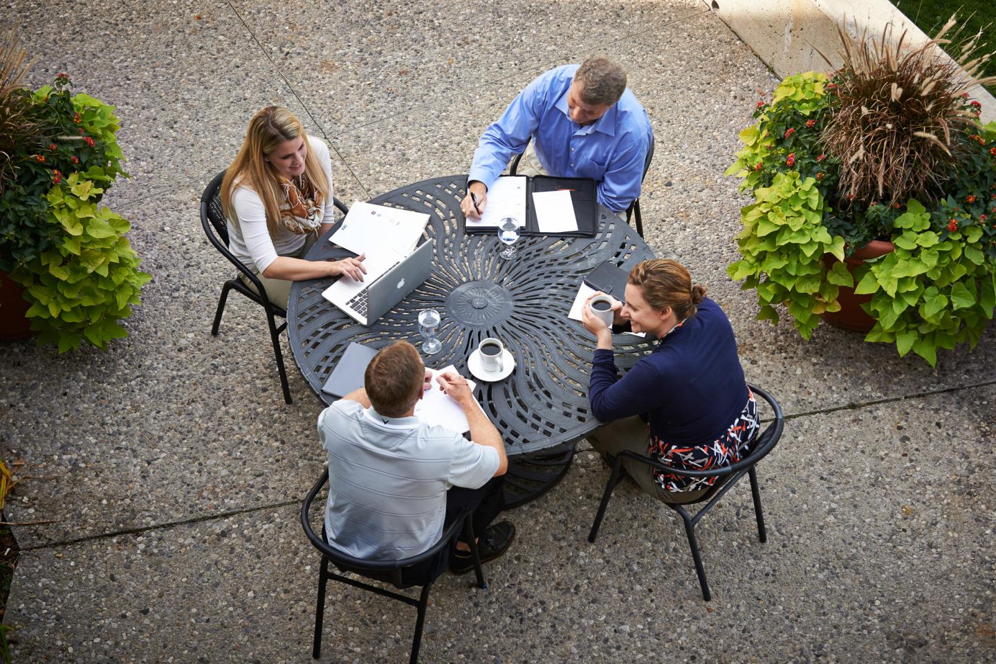 Four people having a meeting at a round table outside, with greenery around.