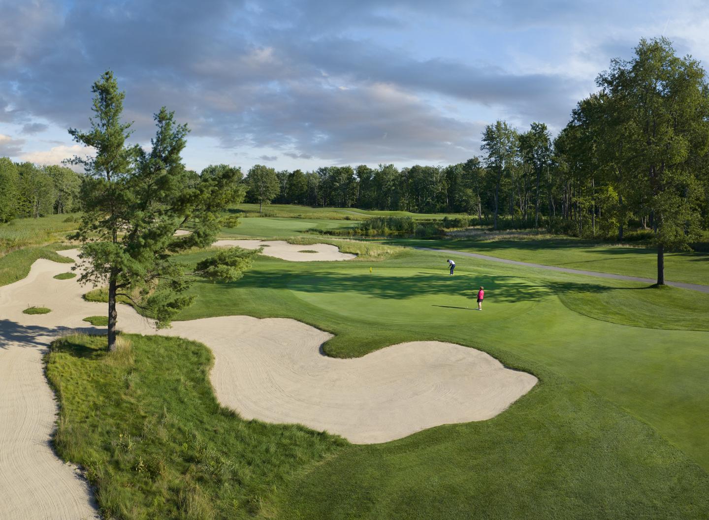 Golf course with sand traps, lush greenery, and cloudy sky.