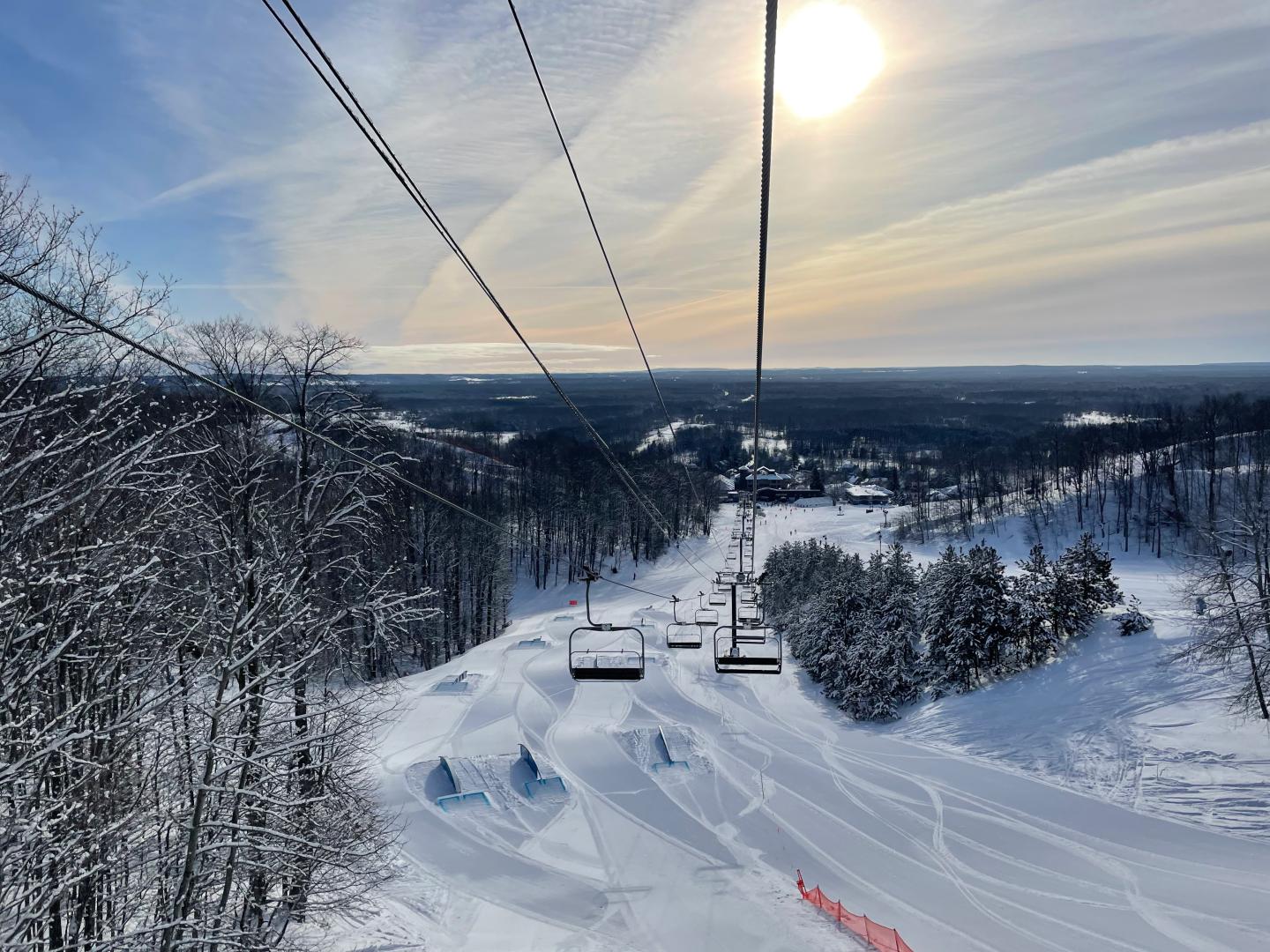 Ski slope with lift, snowy trees, and a bright sun in a clear sky.