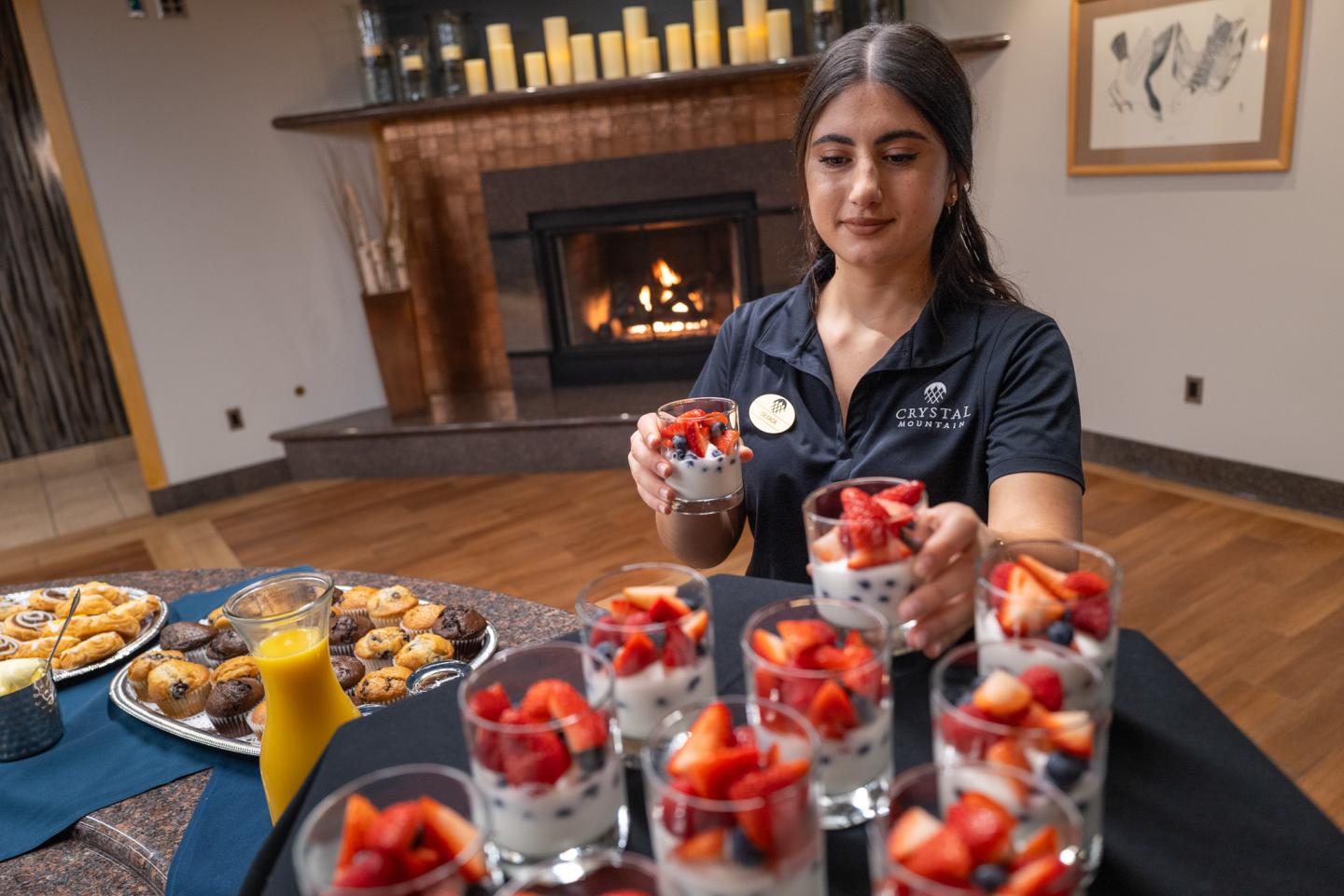 Server arranging fruit parfaits on a table in a cozy room by a fireplace.