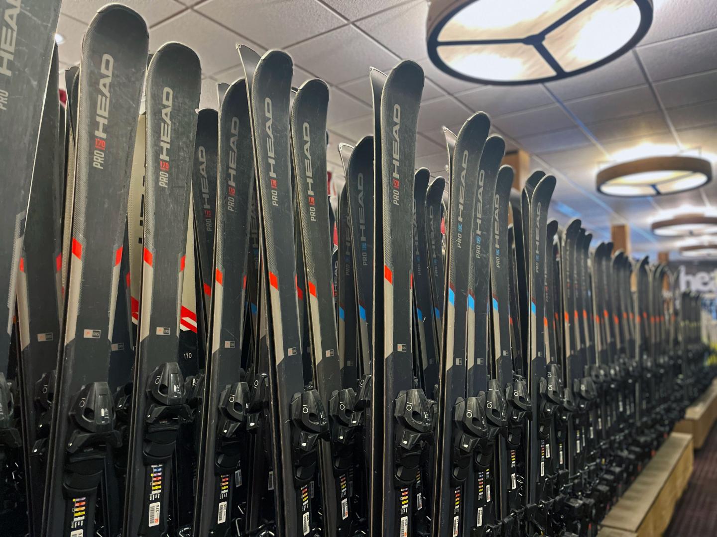 Rows of skis stacked vertically in a shop under bright ceiling lights.