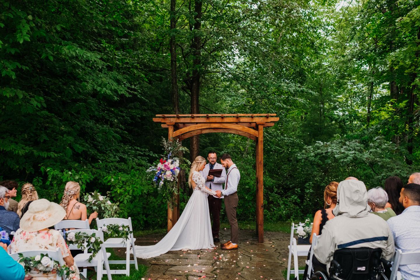 Wedding ceremony in a lush, wooded setting with guests seated.