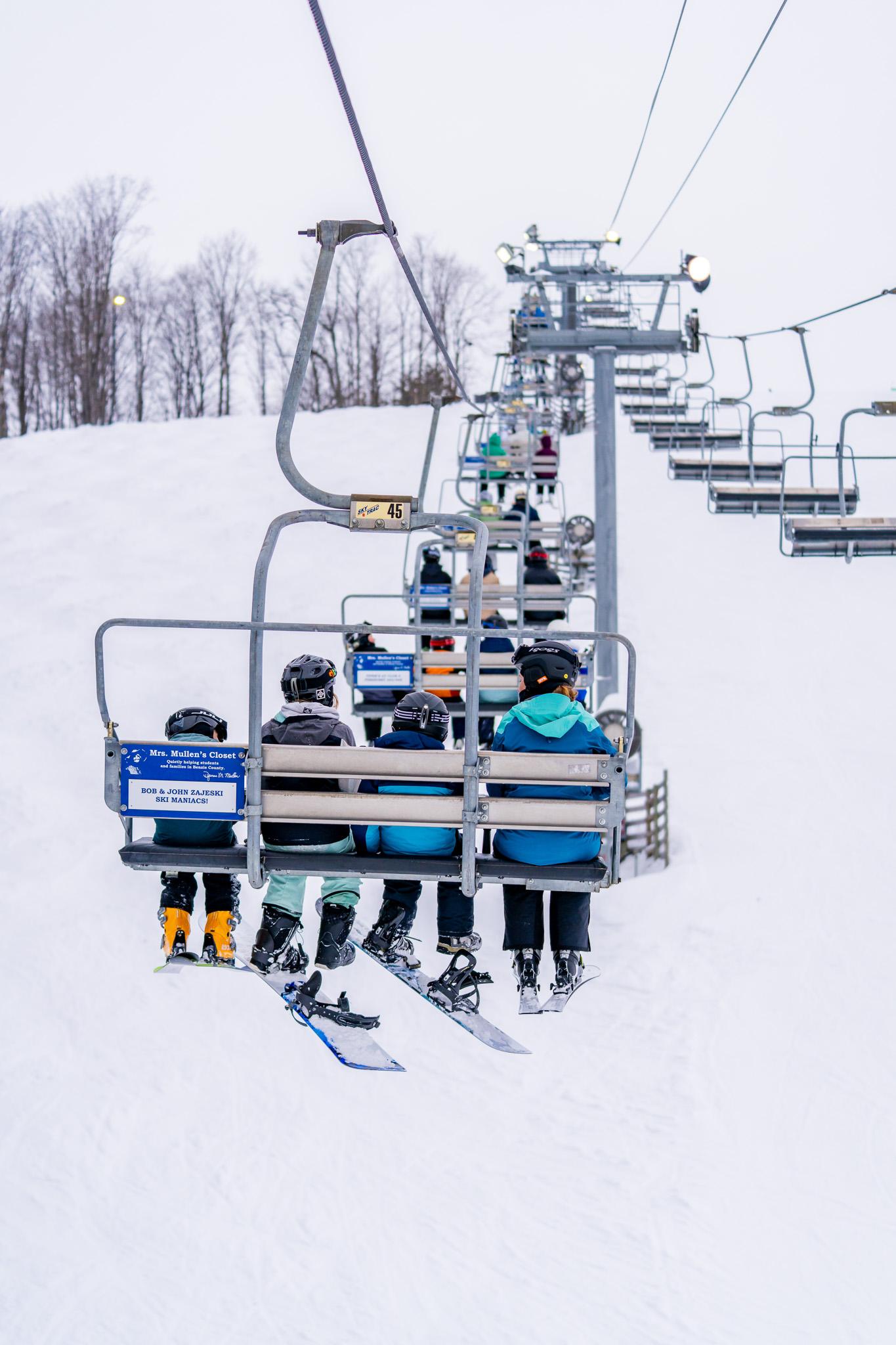 Skiers on a chairlift ascending a snowy slope.