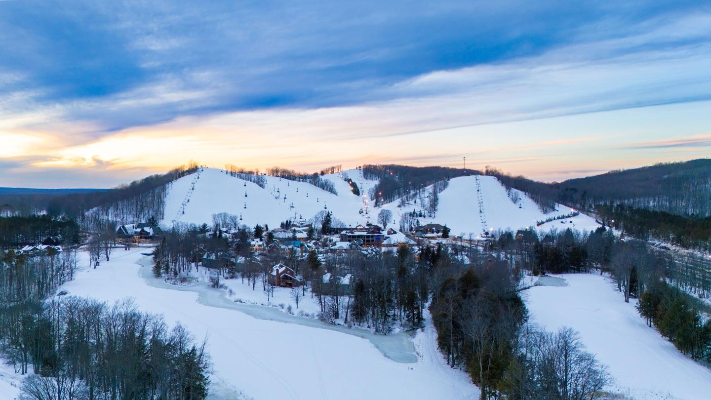 Crystal Mountain aerial photo in winter with hills and trees under a blue sky at sunset.
