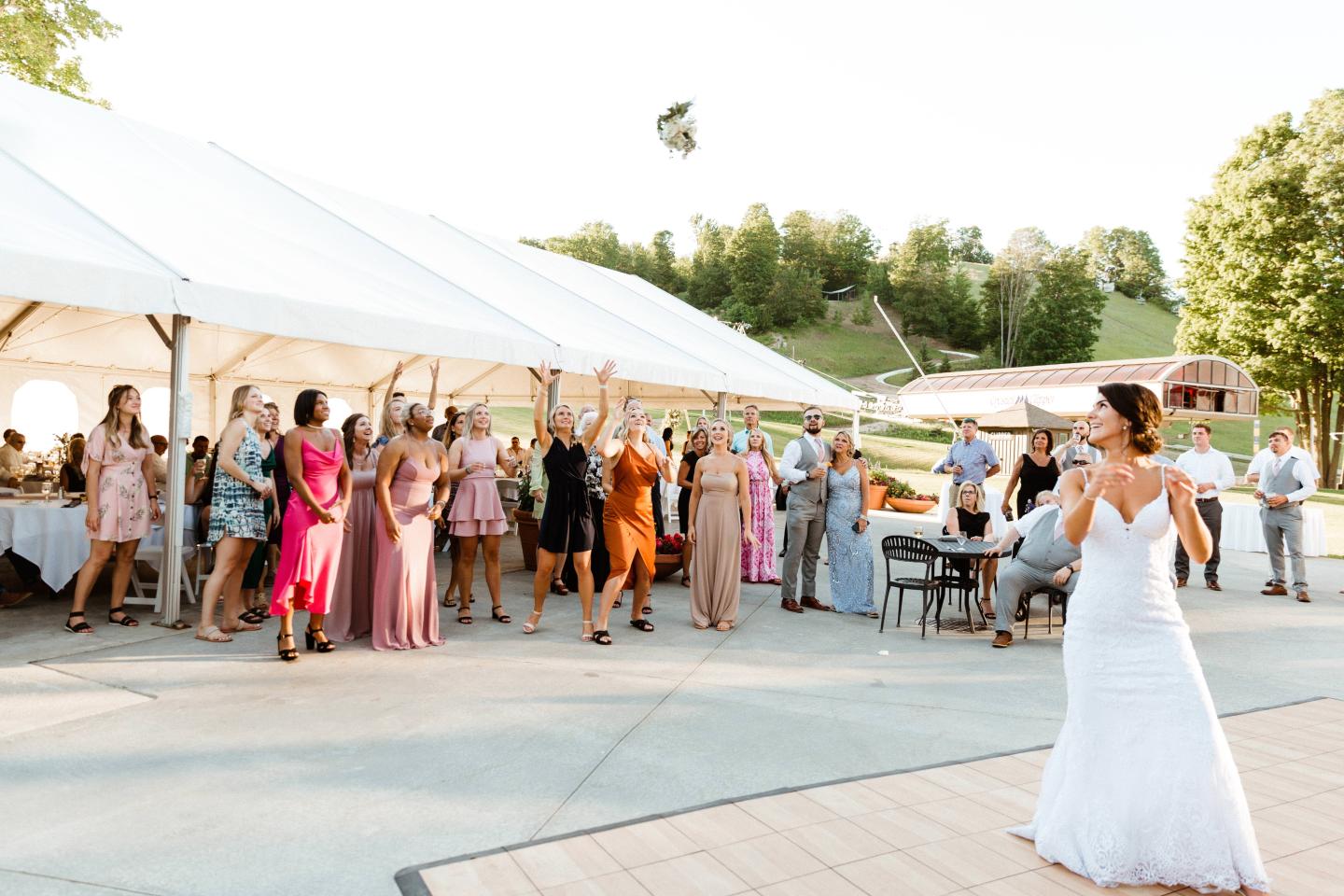 Bride tosses bouquet to guests at outdoor wedding reception.