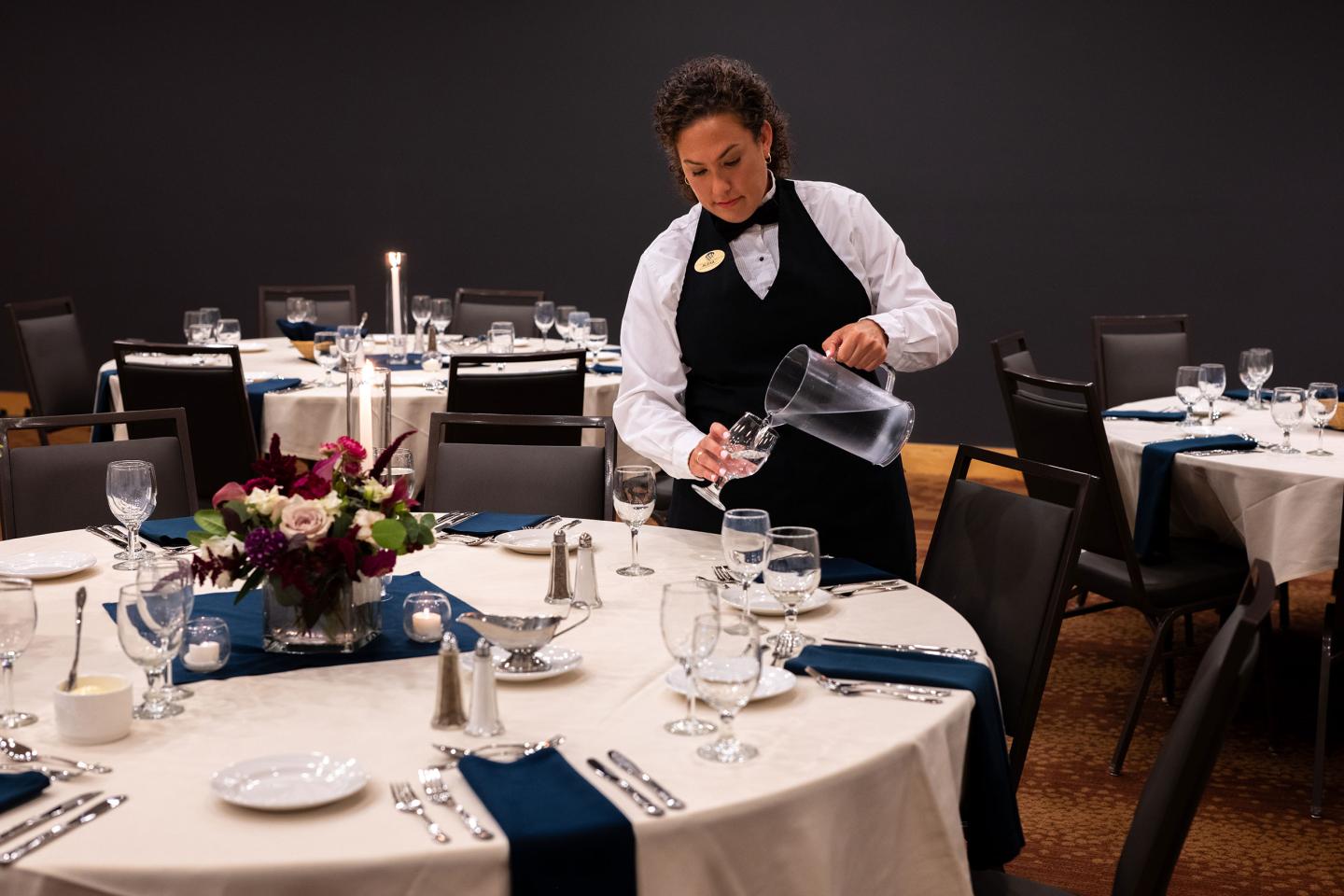 Server in formal attire pouring water at a banquet table.