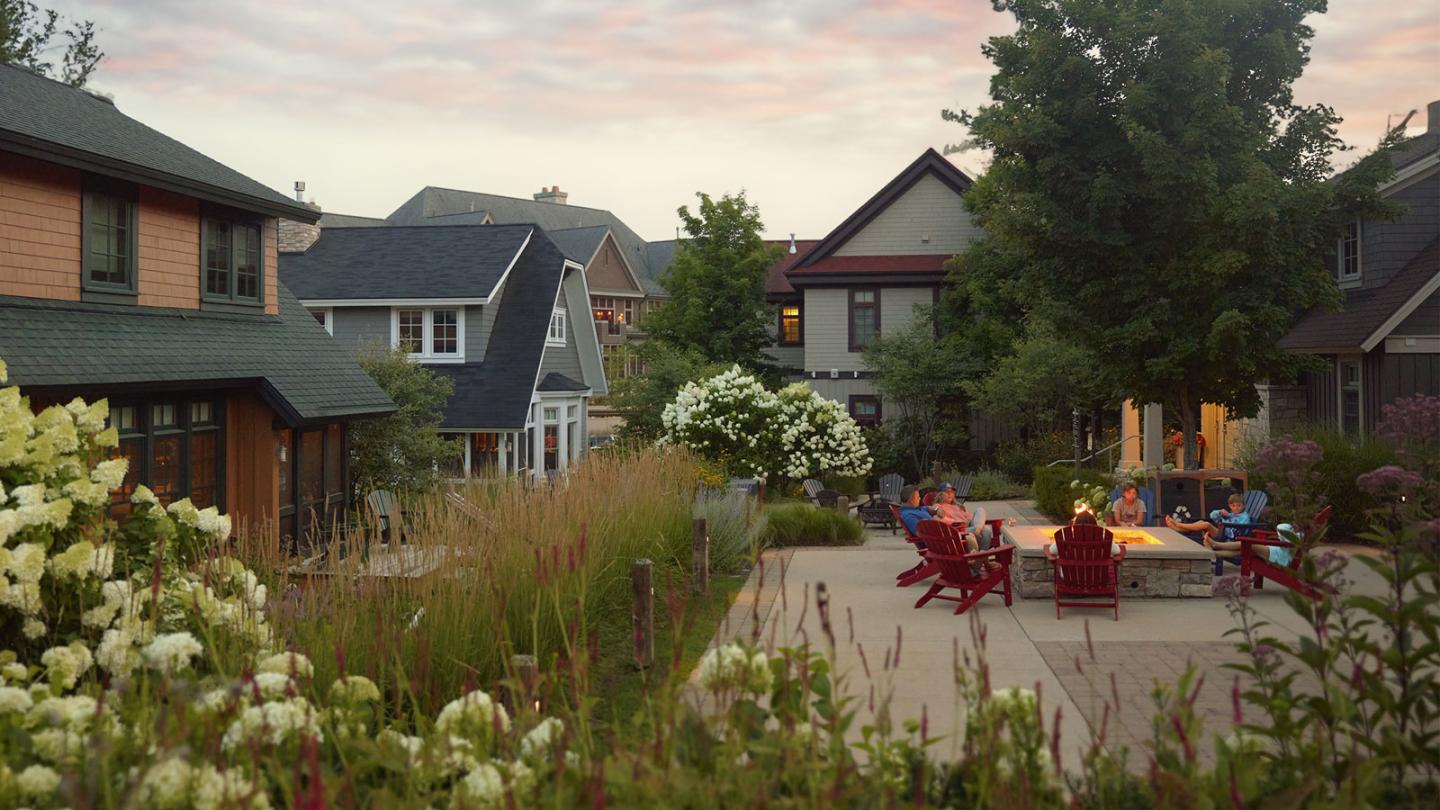 Cozy backyard gathering with chairs, fire pit, flowers, and houses at sunset.