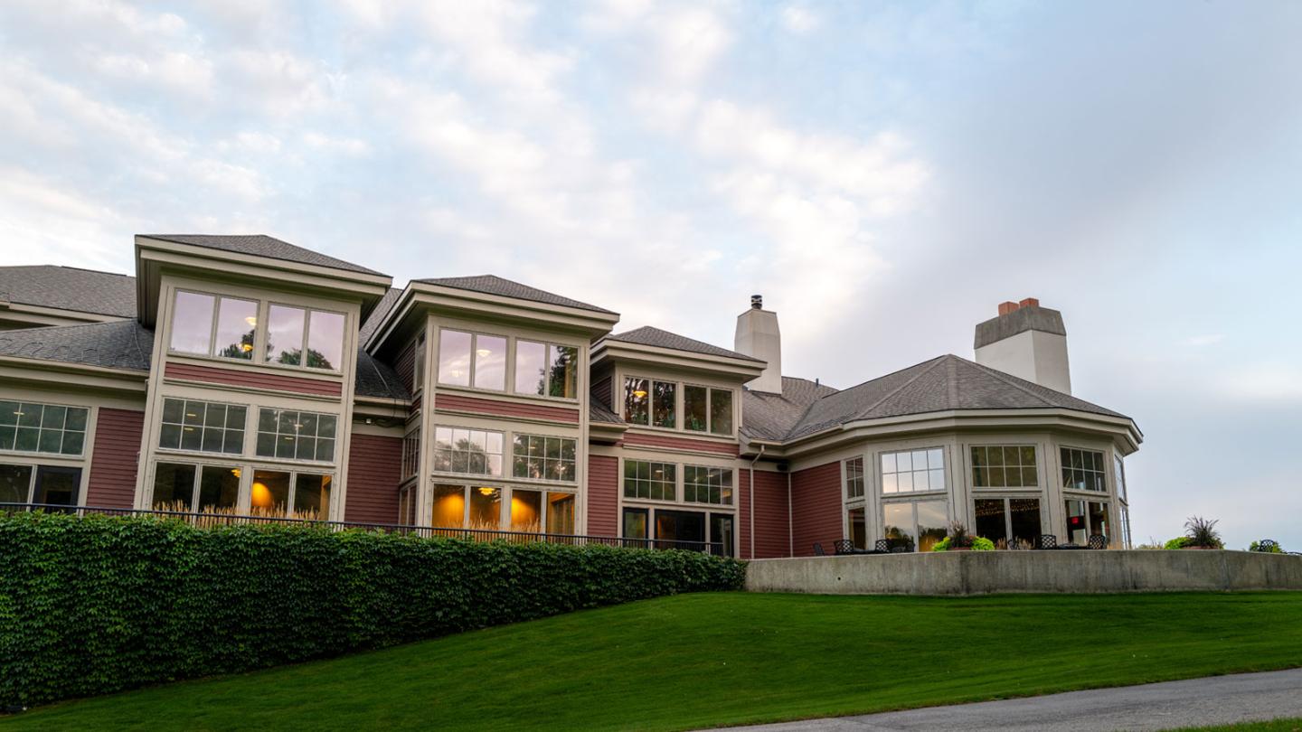 Large house with many windows, surrounded by lush greenery under a cloudy sky.