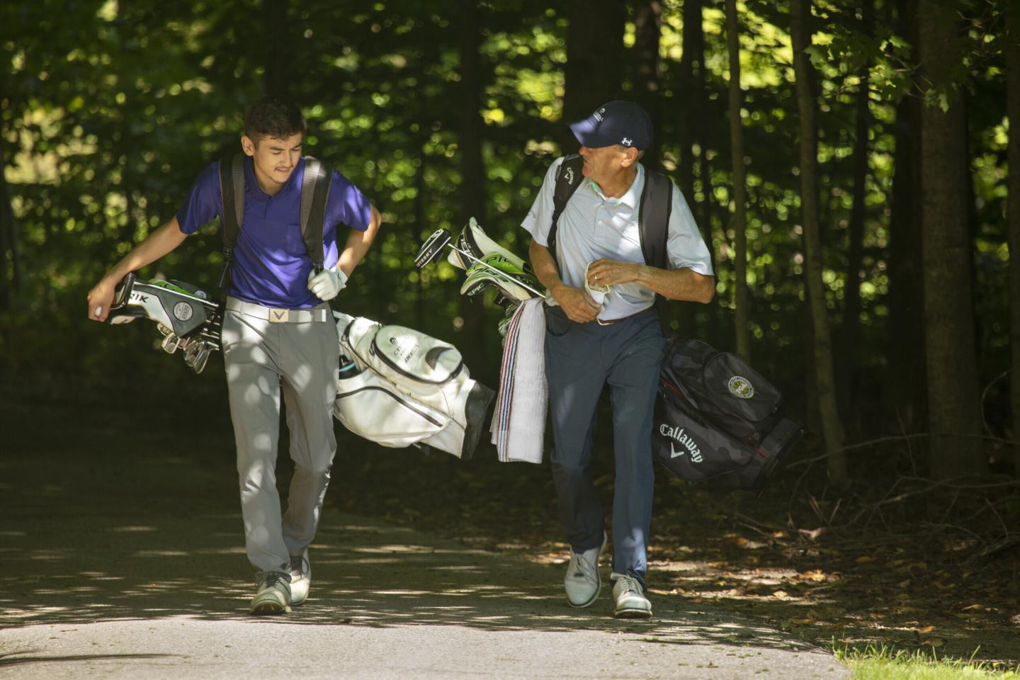 Two people walking on a forest path, carrying golf bags.