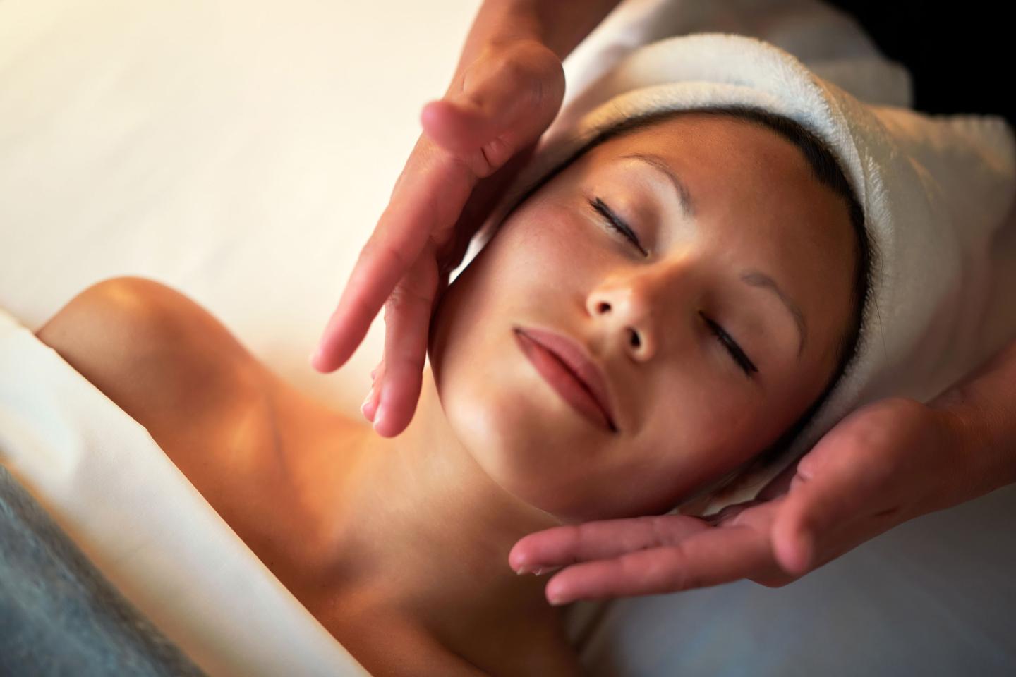 Relaxed woman receiving a facial massage with a towel wrapped around her head.
