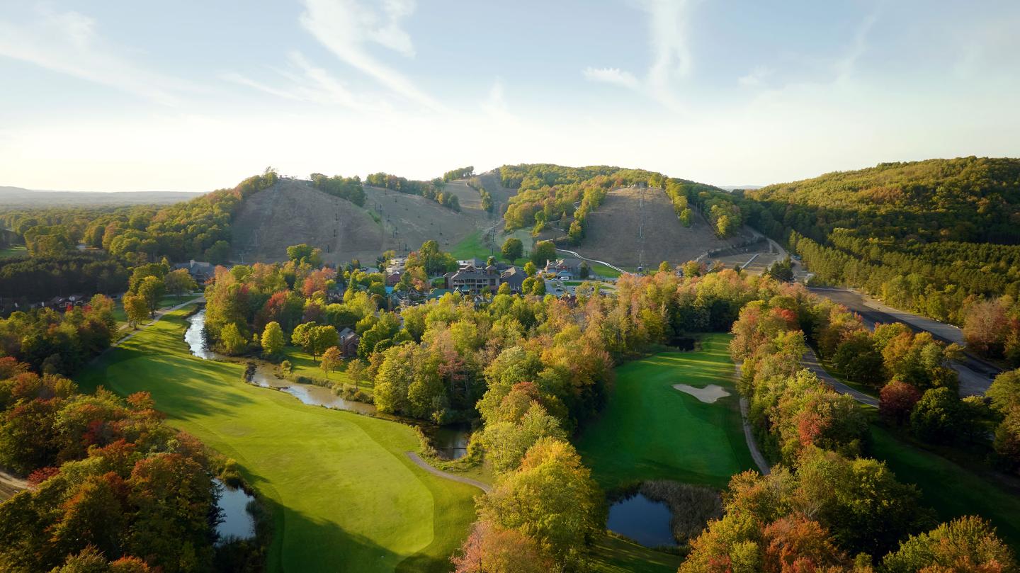 Aerial view of a golf course surrounded by autumn trees and rolling hills.