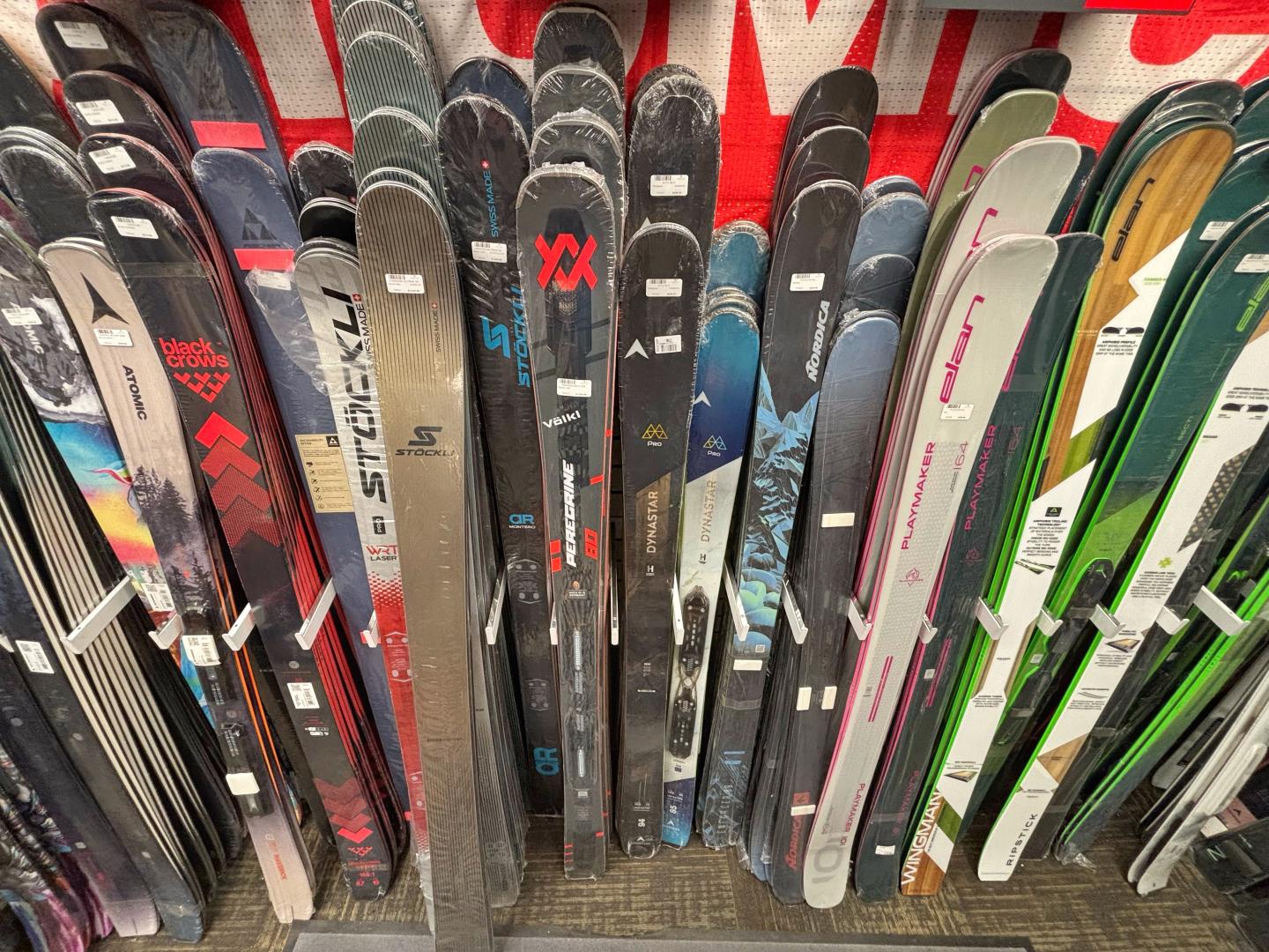 Skis of various colors and brands lined up vertically.