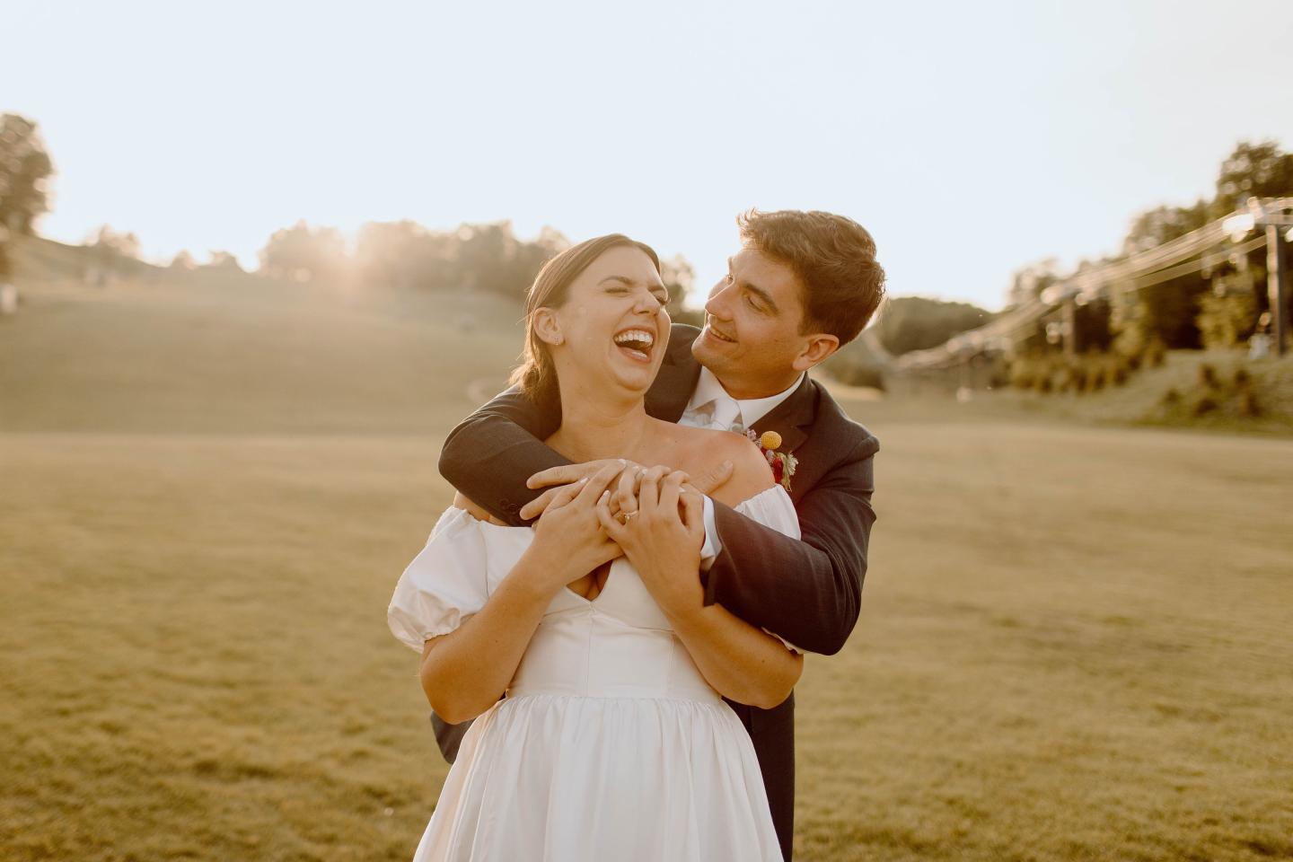 Couple laughing in a field at sunset, embracing warmly.