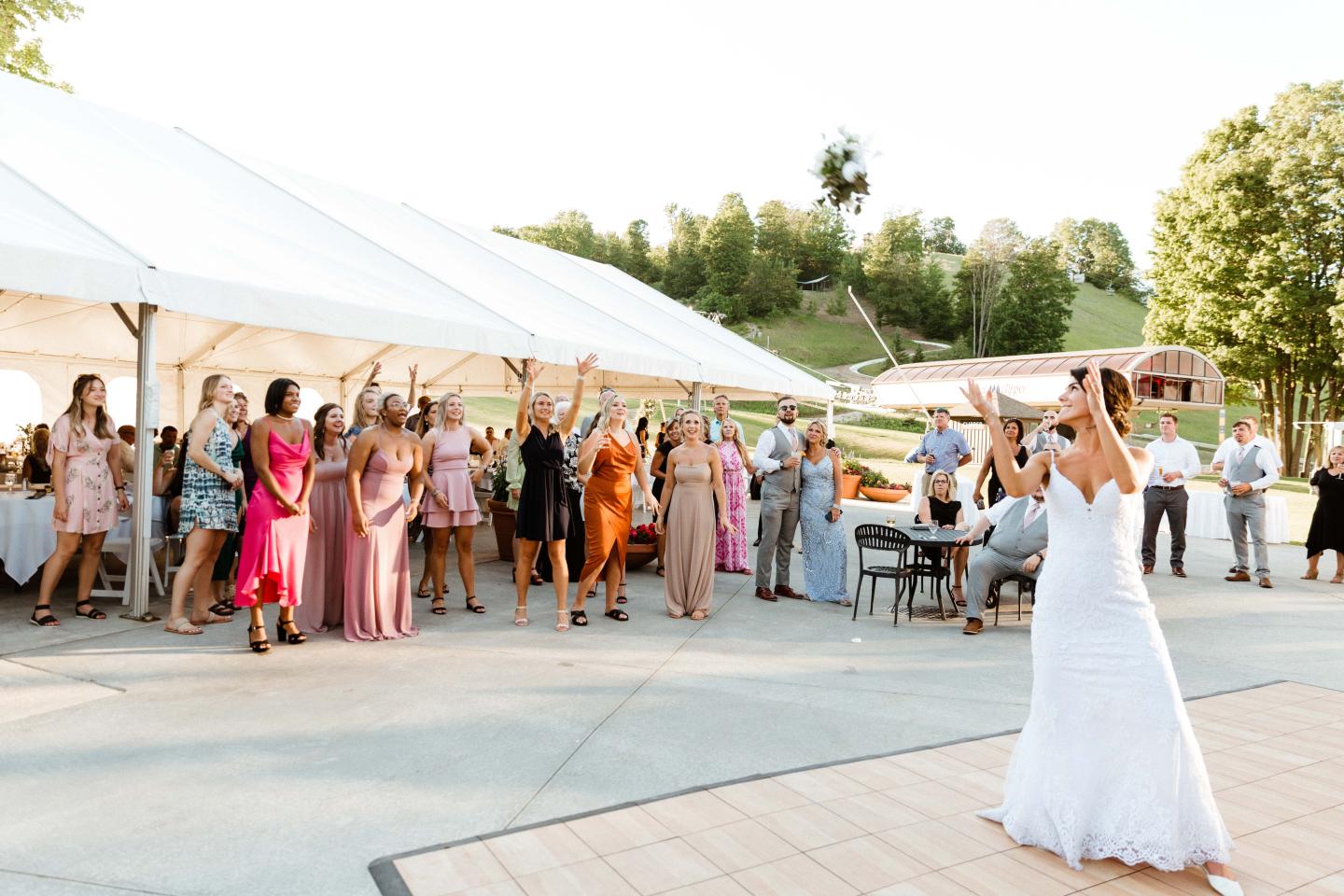 Bride tossing bouquet to crowd at outdoor wedding reception.