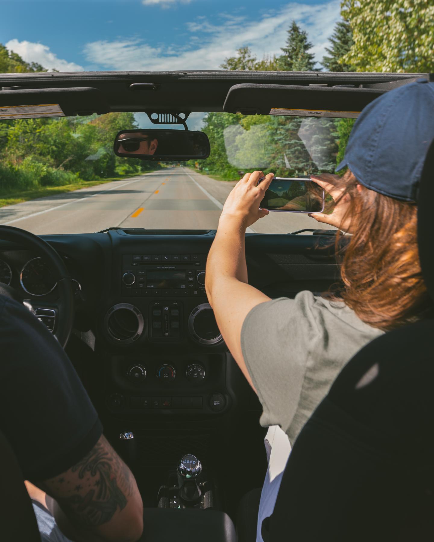 Two people in a convertible driving on a scenic, tree-lined road.