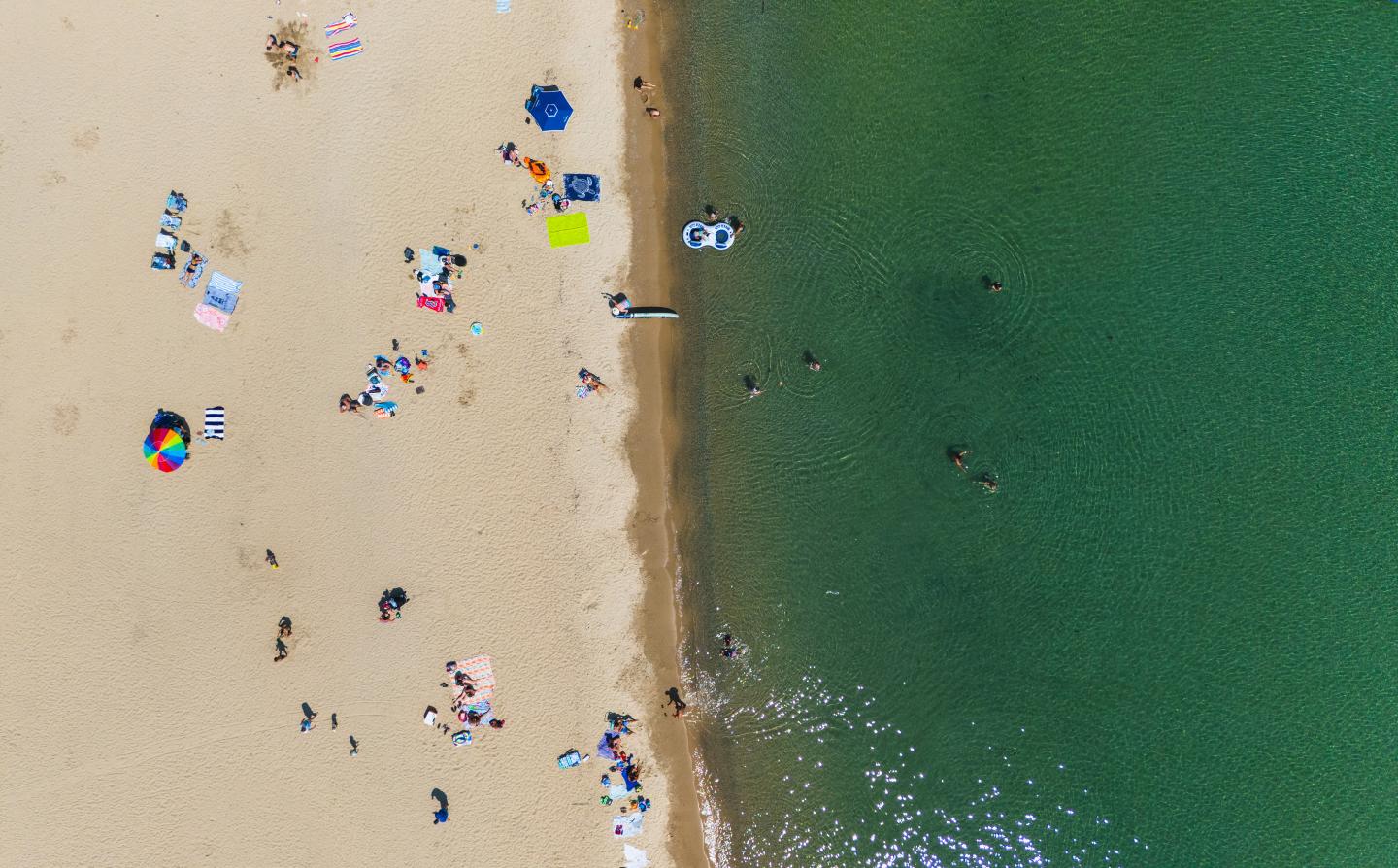 Sandy beach with people and umbrellas next to green water, aerial view.