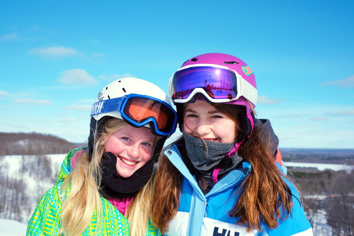 Two smiling skiers in helmets and goggles on a snowy slope.