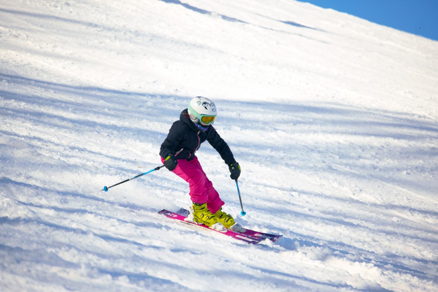 Skier in bright gear descends snowy slope on a sunny day.