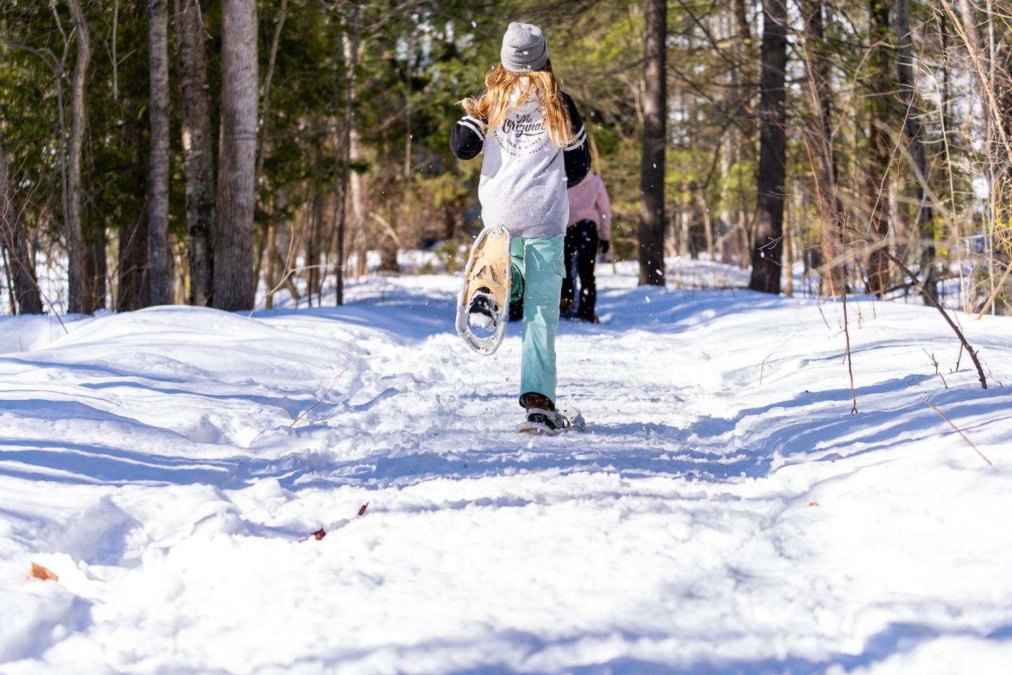 Girl walking on a snowy forest path, wearing a beanie and winter clothes.