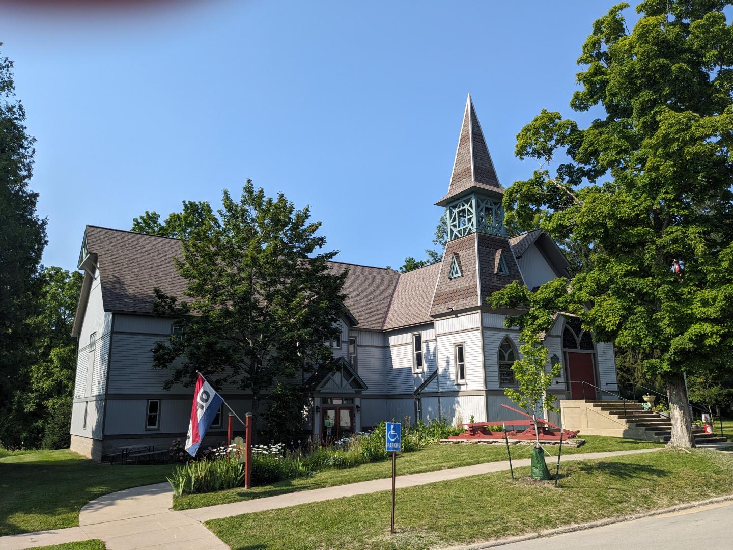 Historic church with a tall steeple, surrounded by trees under a clear blue sky.
