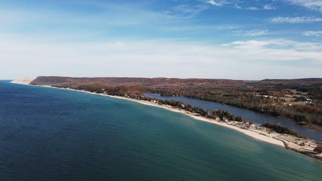 Coastline with sandy beach and forest under a blue sky.