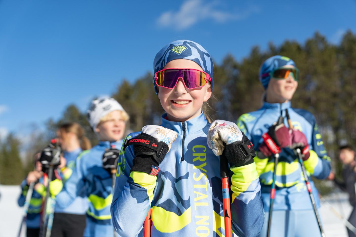 Skiers in bright gear smiling under a clear blue sky.
