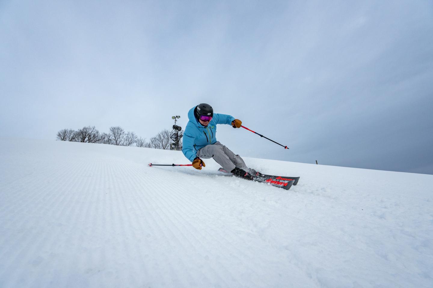 Skier in blue jacket carving down snowy slope under cloudy sky.