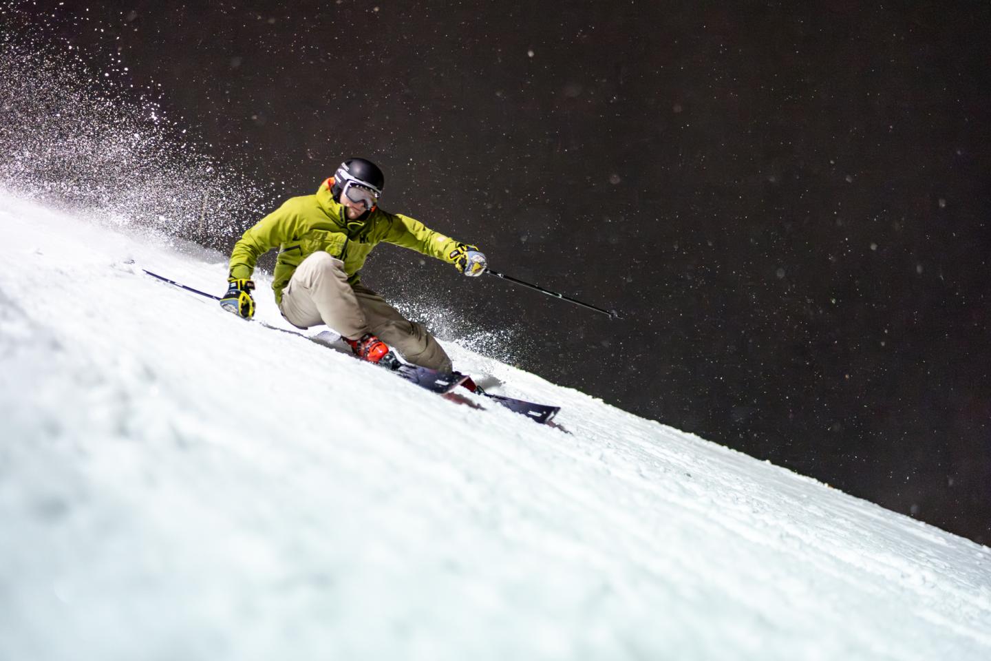 Skier in green jacket descending snowy slope at night.