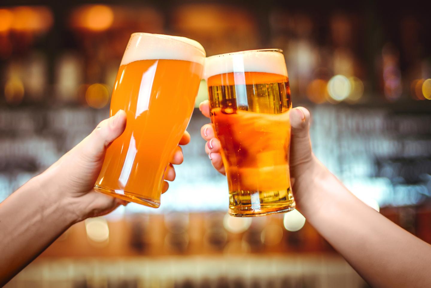 Two hands clinking beer glasses in a bar.