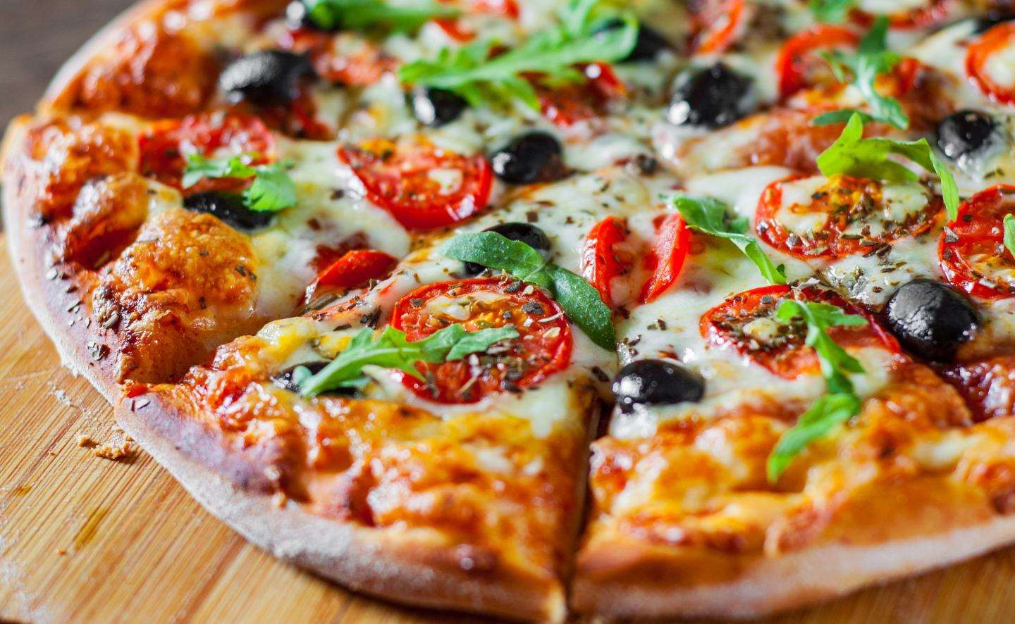 Vegetarian pizza with tomatoes, olives, and arugula on a wooden board.