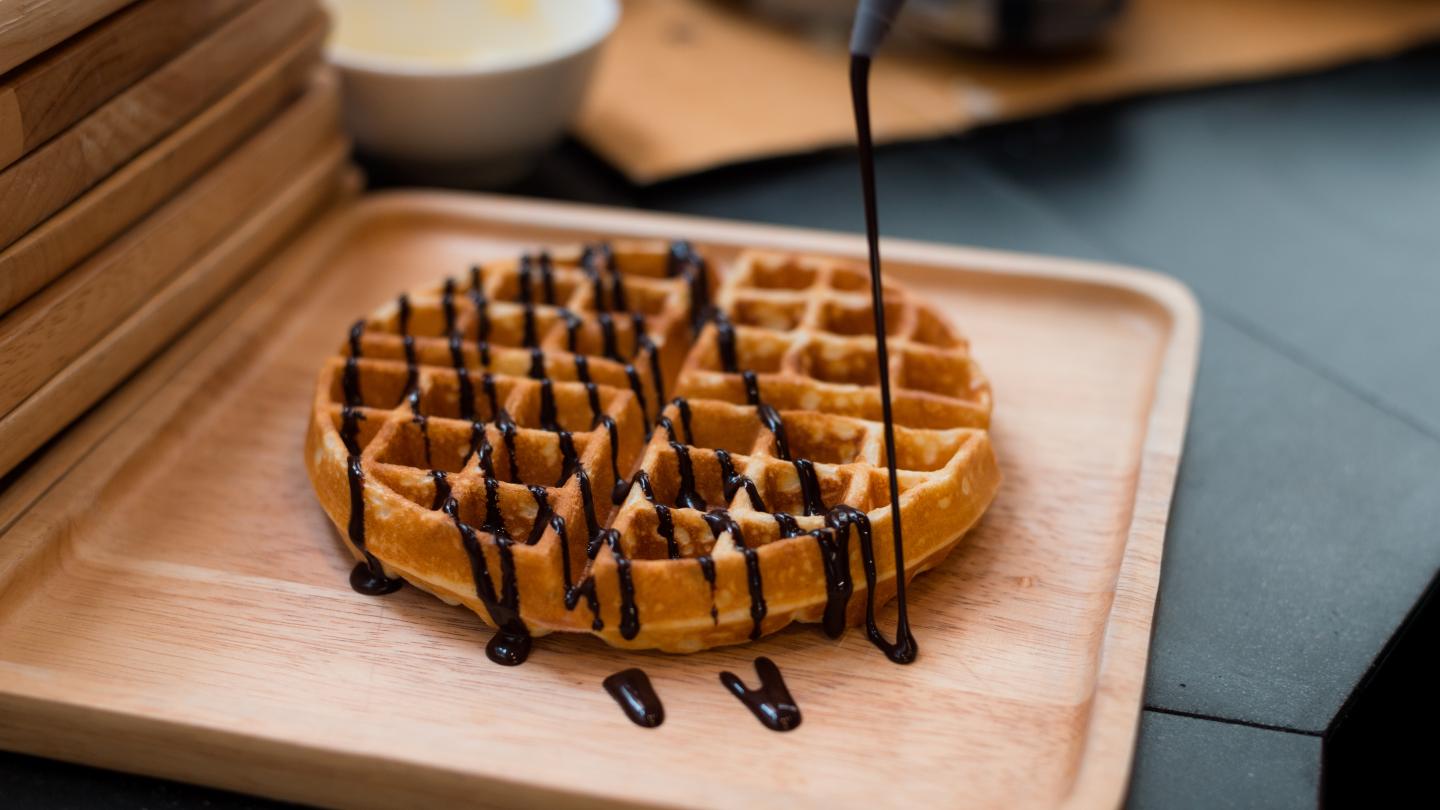Waffle topped with chocolate syrup on a wooden plate.
