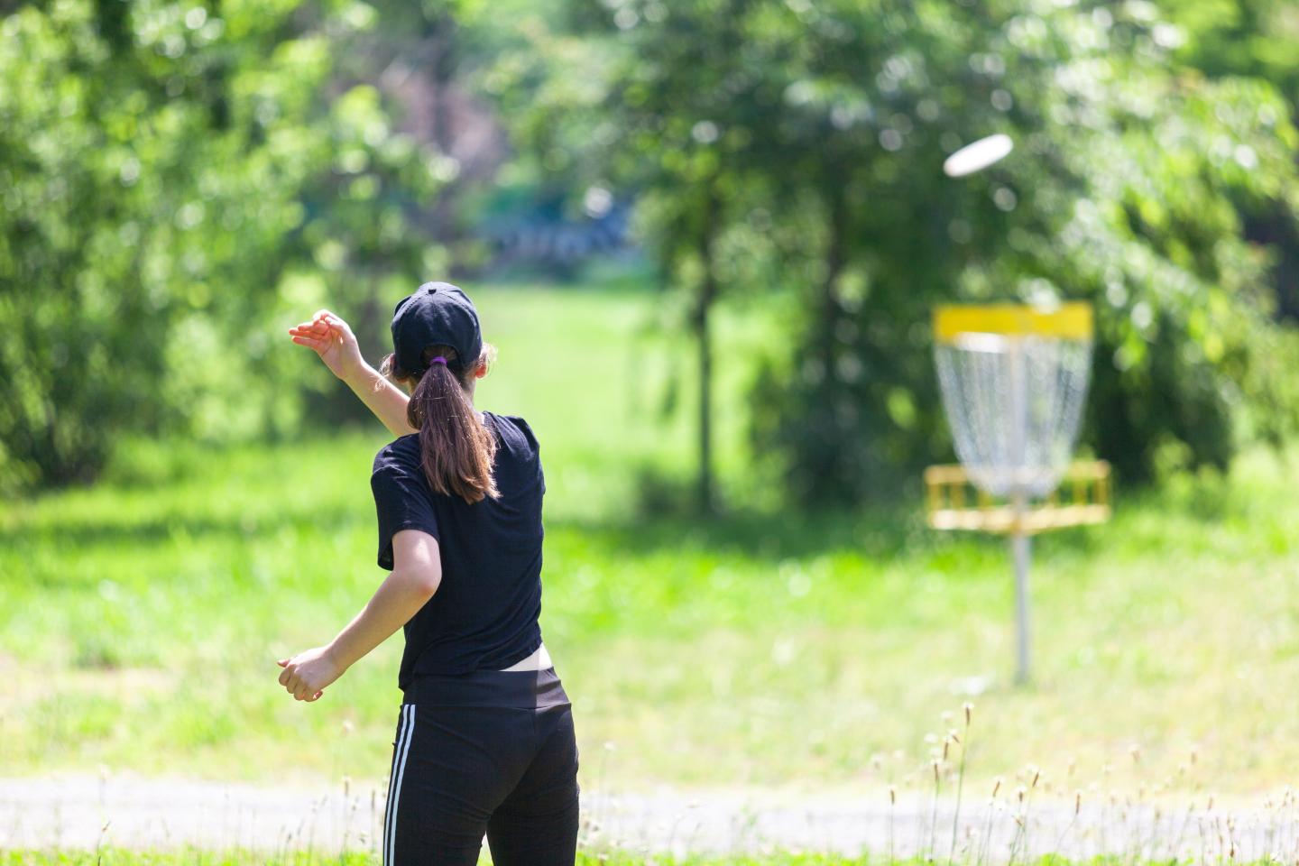 Woman playing disc golf in a sunny park.