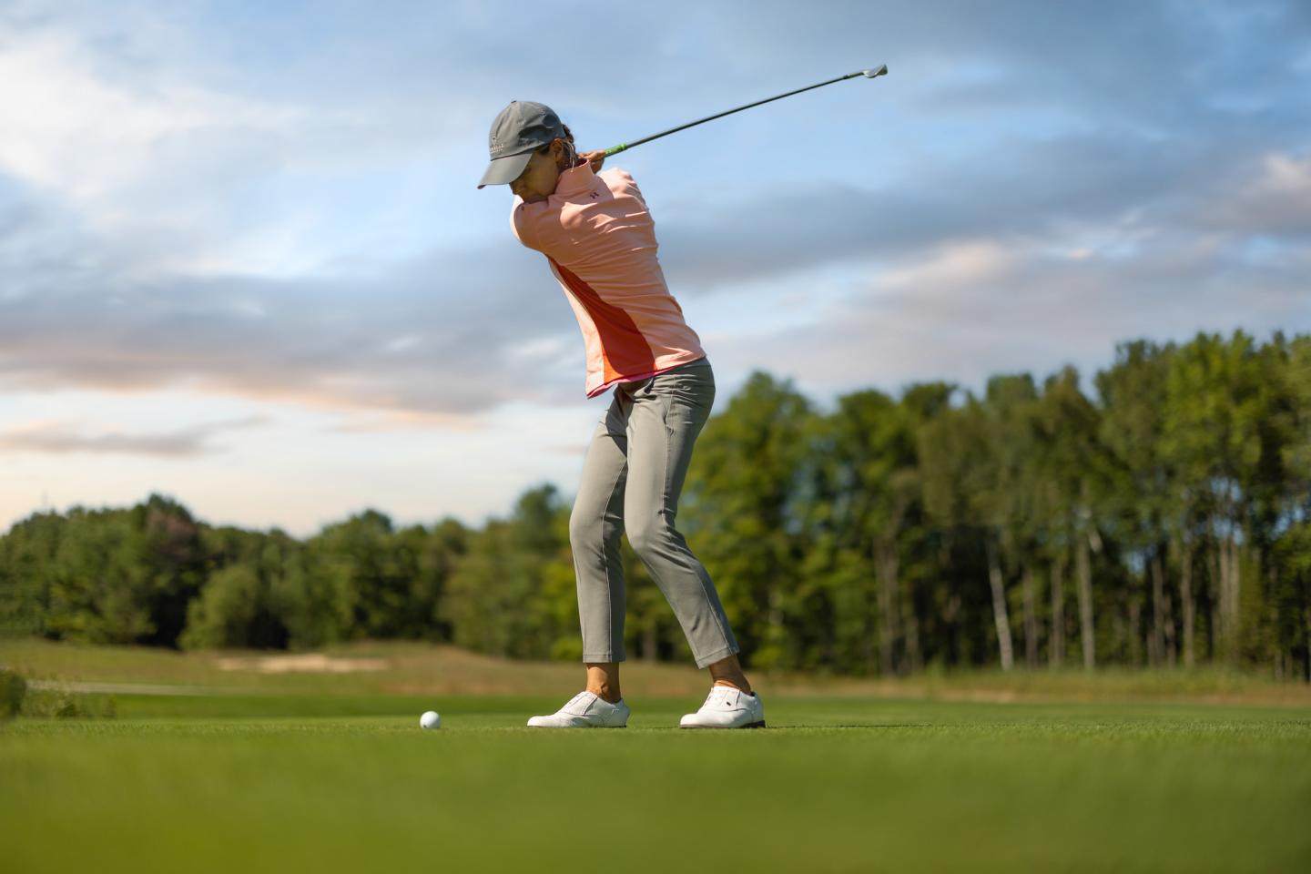 Golfer in mid-swing on a lush green course under a cloudy sky.