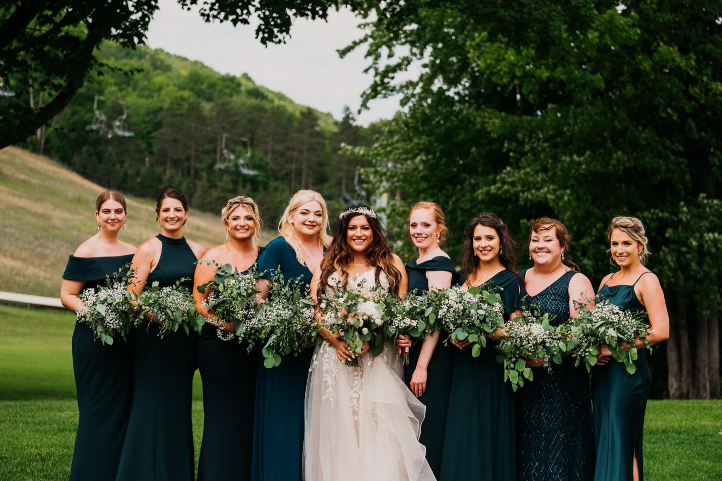 Bridesmaids in teal dresses and bride holding bouquets, standing outdoors.